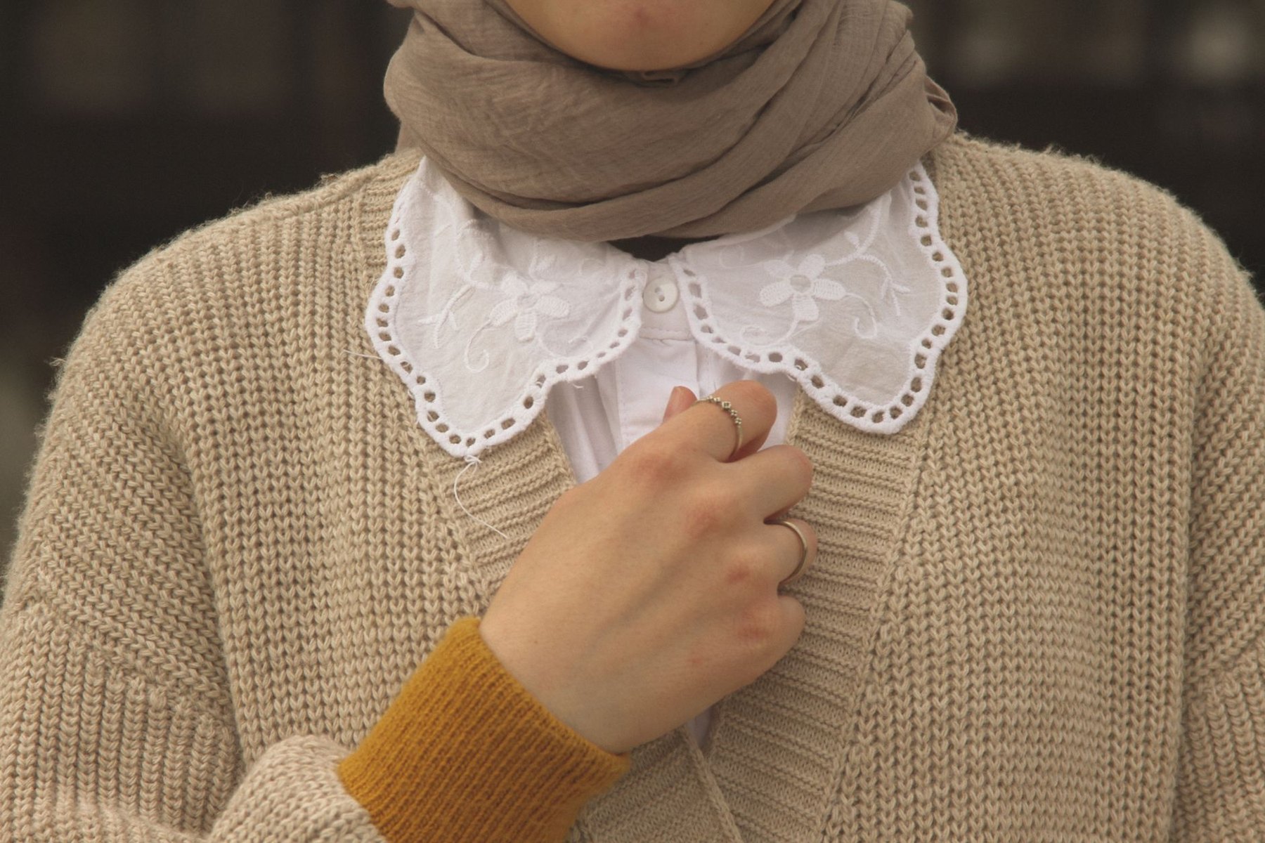 Beige knit cardigan layered over a white blouse with an embroidered collar, worn with a taupe scarf.