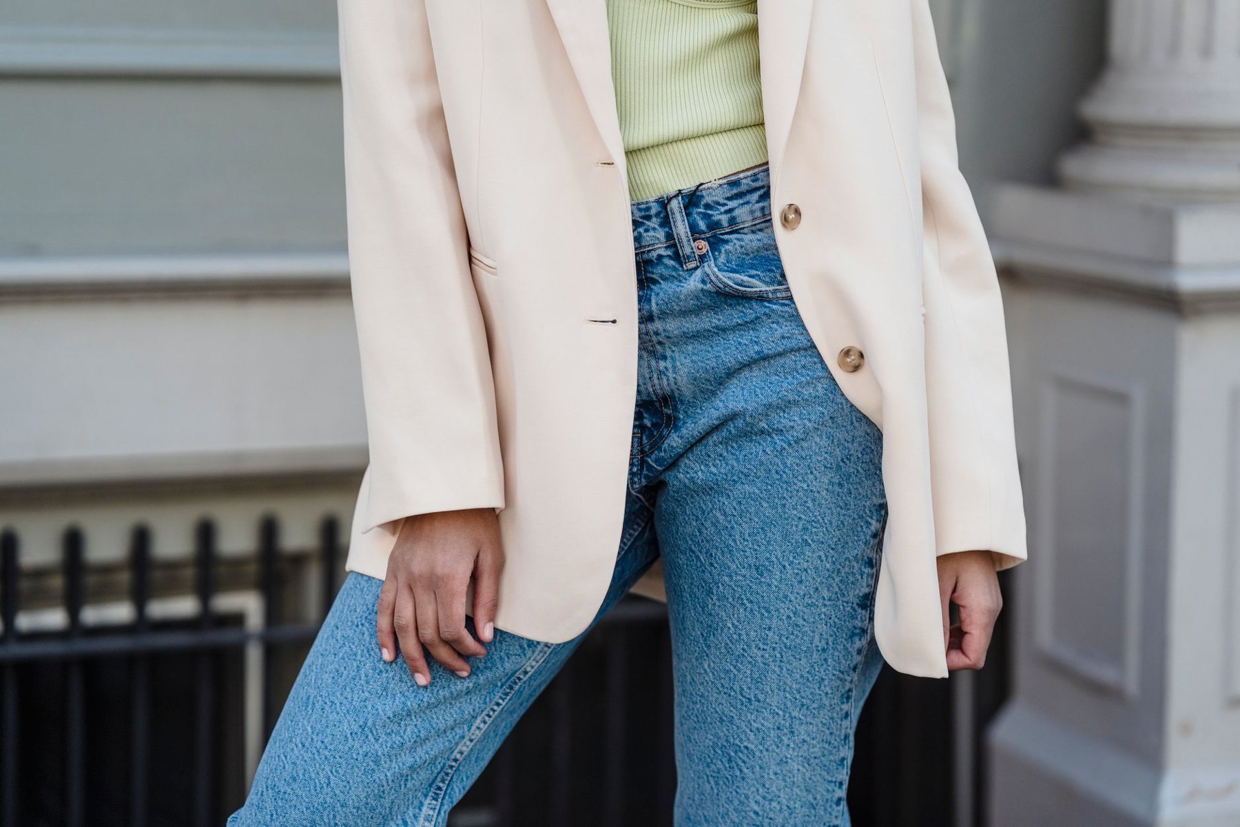 A person wearing a cream blazer over a pale green top with high-rise blue jeans outdoors.