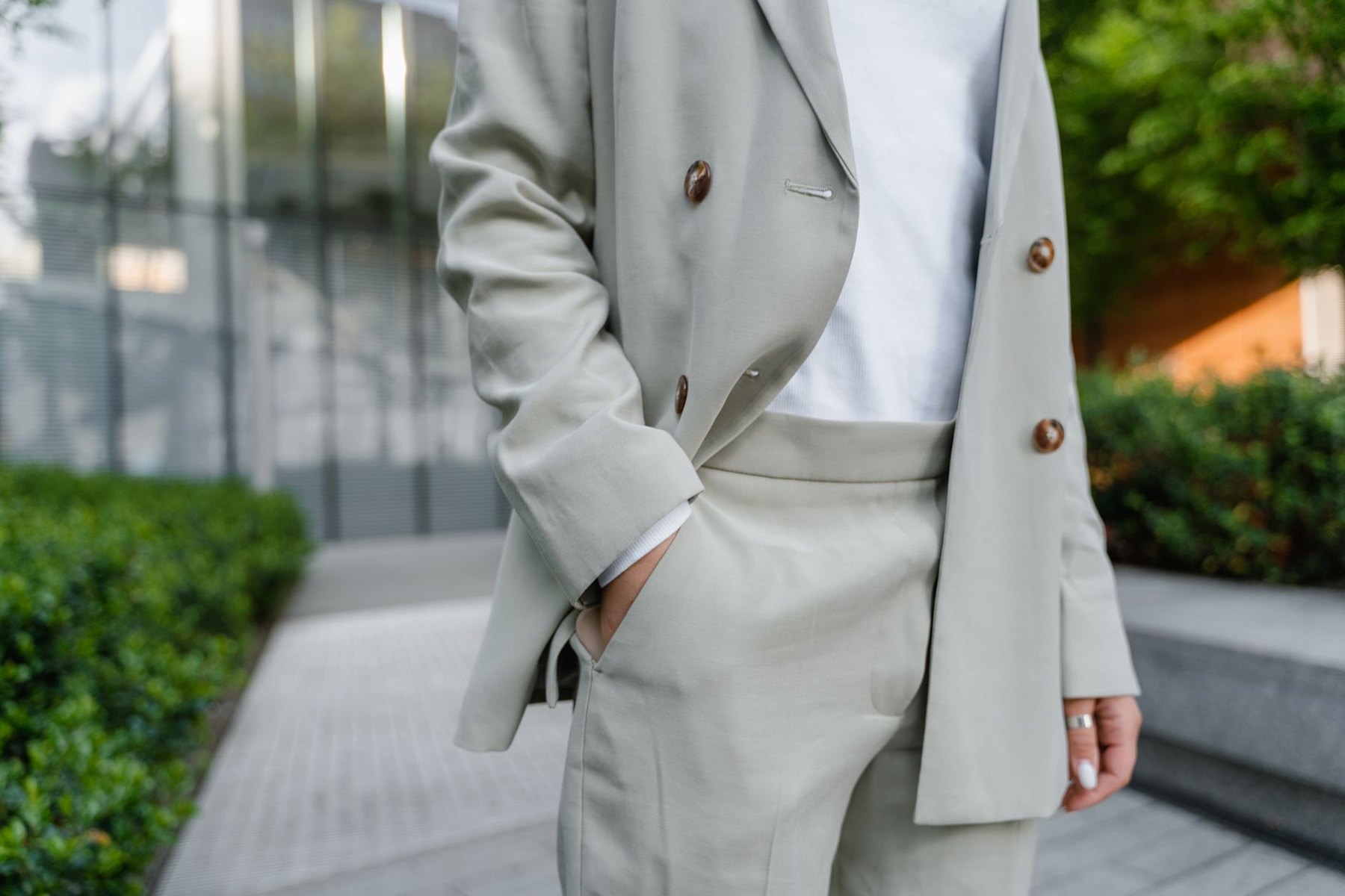Person wearing an open light neutral blazer with matching trousers and a white top outdoors.